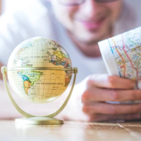 Mann sitzt am Tisch und plant eine Weltreise, Weltkarte und kleiner Globus vor ihm