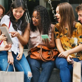 Gruppe Menschen sitzt auf einer Bank und schaut gemeinsam auf ein Tablet