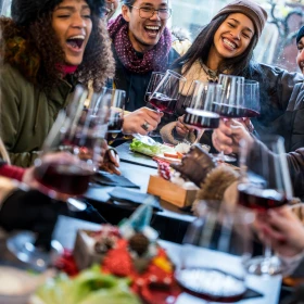 Gruppe feiernde Menschen sitzen an einem Tisch und stoßen mit Weingläsern an