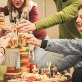 Gruppe Menschen sitzt an einem Tisch und Spiel Jenga, Personen stoßen mit Bier an
