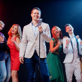 Sänger auf einer Bühne mit Mikrofon im Hintergrund vier lachende und singende Personen