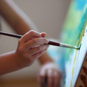 Person malt mit einem Pinsel die feinheiten auf eine Leinwand