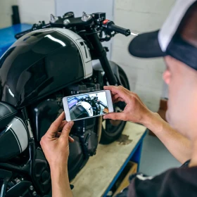 Mann fotografiert ein schwarzes Motorrad mit seinem Handy