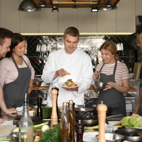 Koch zeigt Gruppe das fertige Gericht