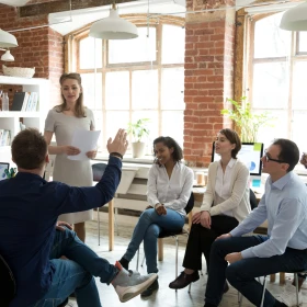 Meeting, Mann meldet sich, Frau steht vor der Gruppe