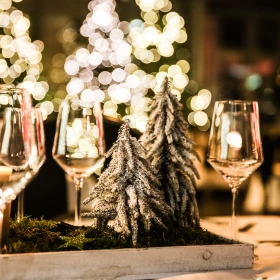 Weingläser auf einem Tisch, Weihnachtsbaum beleuchtet im Hintergrund, Mini-Tanne auf dem Tisch