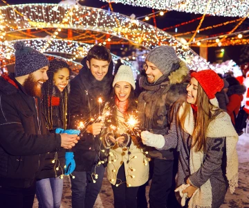 Gruppe steht vor einem Weihnachtsmarkt und hat Wunderkerzen in der Hand