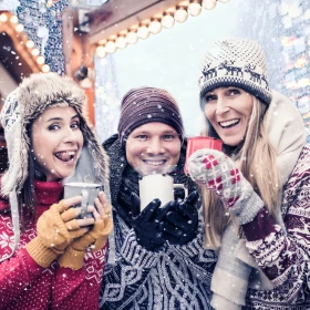 Drei Personen mit Glühwein in der Hand stehen im Schnee und machen ein Gruppenbild, alle lachen