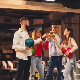 Gruppe hält Bowlingkugel und stößt mit Bier an
