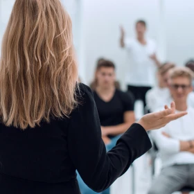 Frau hält einen Workshop und steht frontal vor den Teilnehmern