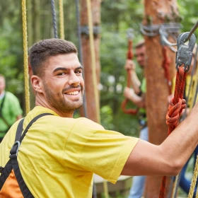 Mann mit gelben T-Shirt im Kletterwald in einer Übung