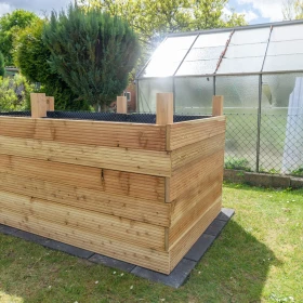 Hochbeet Rohbau mit Folie im Innenbereich auf einer Wiese stehend vor einem Gewächshaus