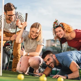 Vier Personen beim Golfspielen schauen, welcher Golfball näher am Loch liegt. Freude, Personen lachen