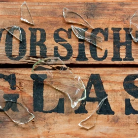 Holz mit Aufschrift "Vorsicht Glas", Glasscherben auf dem Holz