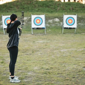 Frau schießt mit einem Bogen auf die Zielscheibe im Hintergrund