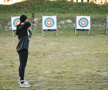 EVINTA_Teamski Sommerbiathlon mit Bogenschießen_Bild01 Frau schießt mit einem Bogen auf die Zielscheibe im Hintergrund