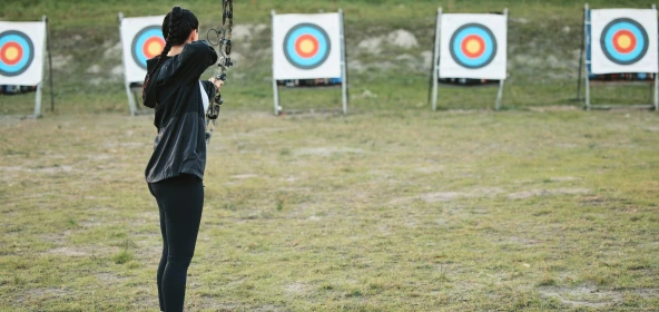 Frau schießt mit einem Bogen auf die Zielscheibe im Hintergrund