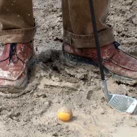Golfball vor Füßen im Sand