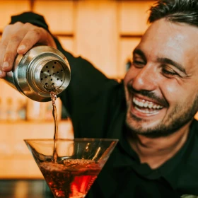 Lachender Mann schenkt Cocktail in ein Glas