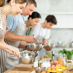 Vier Personen kochen gemeinsam und tragen weiß-braun gestreifte Kochschürzen