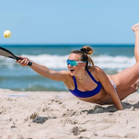 Frau im Sand am Meer spielt Tennis am Strand