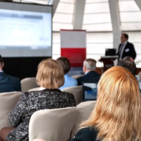 Tagung, Stuhlreihen, Teilnehmer schauen auf eine Leinwand, Vortrag wird gehalten