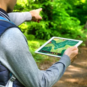 Mann läuft mit einem Tablet in de Hand durch einen Wald und zeigt den Weg