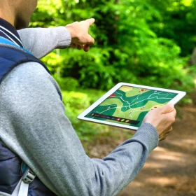 Mann läuft mit einem Tablet in de Hand durch einen Wald und zeigt den Weg