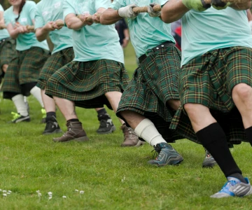 5 Menschen mit Schottenröcken ziehen an einem Seil beim Seilziehen