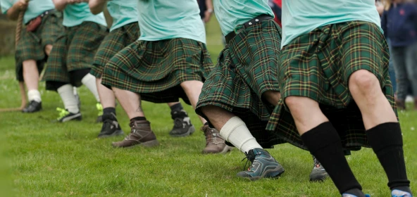 5 Menschen mit Schottenröcken ziehen an einem Seil beim Seilziehen