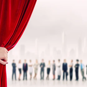 Personen stehen auf einer Bühne, ein roter Vorgang wird aufgehalten