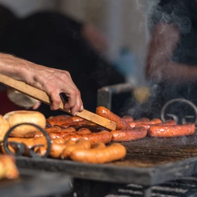 Person wendet die Bratwürste auf dem Grill