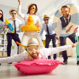 Geschäftsleute verkleidet für den Sommerurlaub. Ein Mann trägt eine Schwimmbrille und einen Sonnenhut und liegt auf einer Luftmatratze auf dem Büroboden.