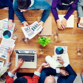 Personen sitzen an einem Holztisch, Laptop, verschiedene Grafiken in den Händen