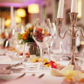 Tafel mit weißer Tischdecke, eingedeckt mit Geschirr und Besteck, goldener Kerzenleuchter in der Mitte mit weißen Kerzen