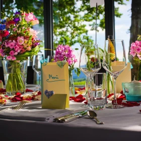 sommerlich eingedeckte Tafel mit bunten Blumen, farbenfroher Dekoration und Menükarten