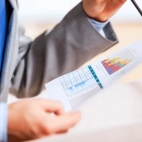 Nahaufnahme eines Redners mit einem Papier in der Hand. Das Papier zeigt eine Grafik und eine Tabelle