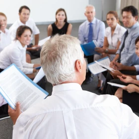 Besprechung mit neun Personen, ein Mann hält einen Vortrag