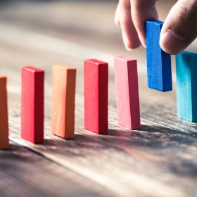 Person setzt einen letzten Stein in eine Domino Reihe ein