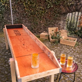 Ein mittelalterlich inszeniertes Krugschieben unter einem roten Pavillon lädt zum Mitmachen ein. Holzelemente, Bierkrüge und Naturmaterialien sorgen für eine warme, einladende Stimmung. Dieses Bild eignet sich perfekt zur Darstellung geselliger Spielstationen auf historischen Events.