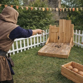 Ein Teilnehmer in mittelalterlicher Gewandung wirft ein Hufeisen auf ein Ziel in einer umzäunten Spielstation. Die Umgebung wurde von modern zu historisch umgestaltet, um eine stimmige Ritterturnier-Atmosphäre zu schaffen. Das Bild zeigt ein klassisches Geschicklichkeitsspiel mit Bewegung und Fokus.