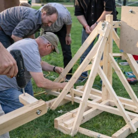 Zwei Männer schrauben an einem Katapult und bauen es zusammen