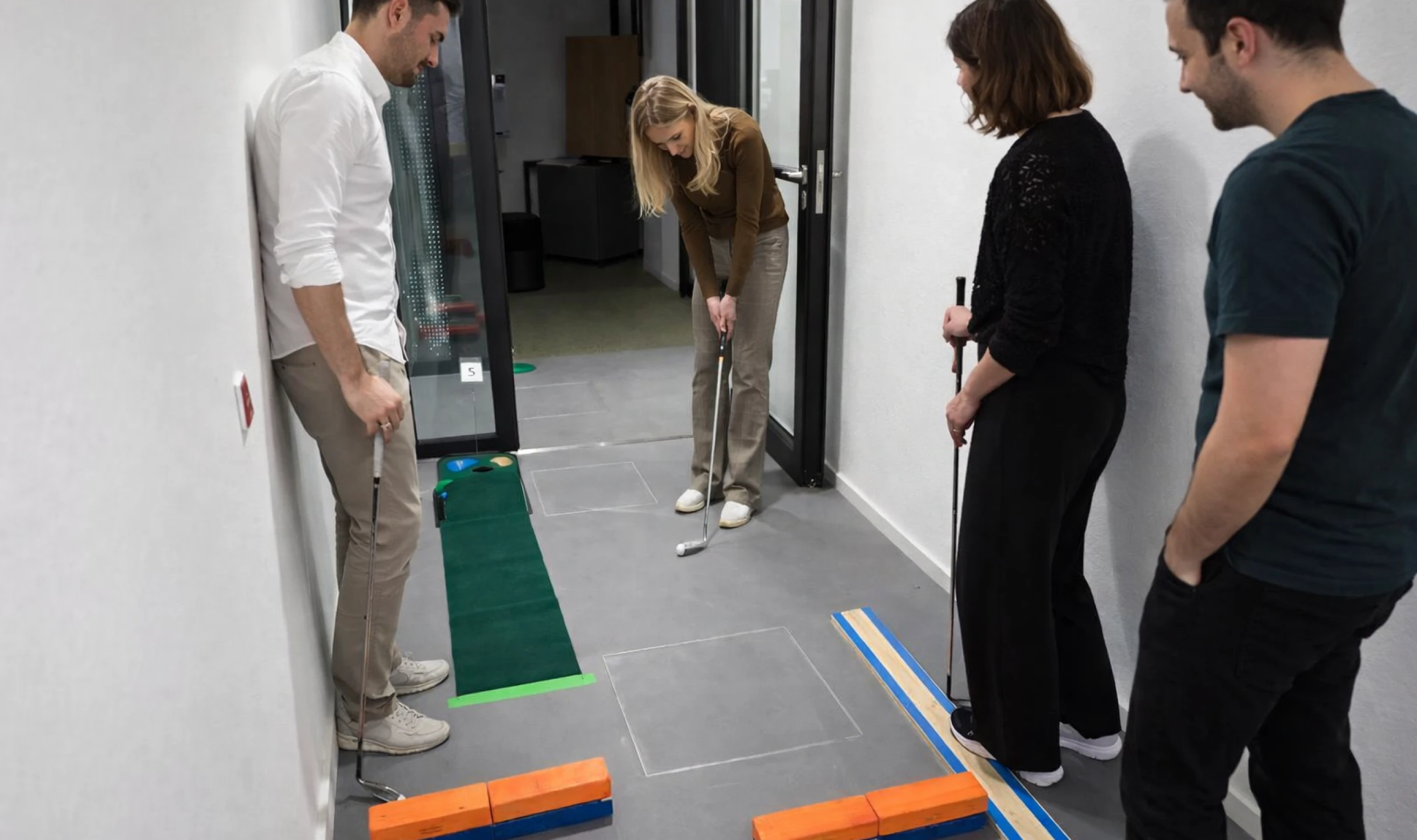 Personen versuchen einen Golfball durch verschiedene Hindernisse zu spielen im Flur des Büros