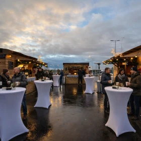 3 Holzhütten weihnachtlich geschmückt, davor weiße Stehtische