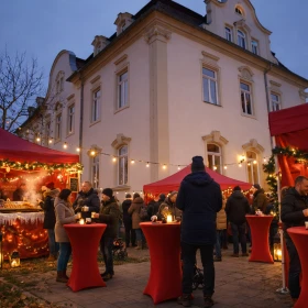 Weihnachtsmarkt mit roten Zelten und Stehtischen vor einem Gebäude