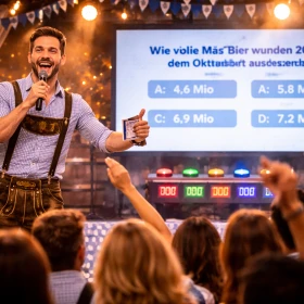Ein Moderator präsentiert auf der Bühne das Oktoberfest-Teamquiz und sorgt für Spannung, Dynamik und professionelle Durchführung des Firmenevents. Das interaktive B2B-Event schafft Motivation, Teambuilding und ein gemeinsames Erlebnis für Unternehmen.