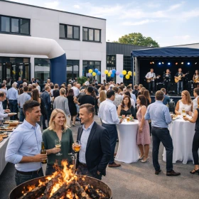 mehrere Personen auf einem Firmenfest auf dem betriebsgelände mit Stehtischen, Feuerschalen und Live Musik
