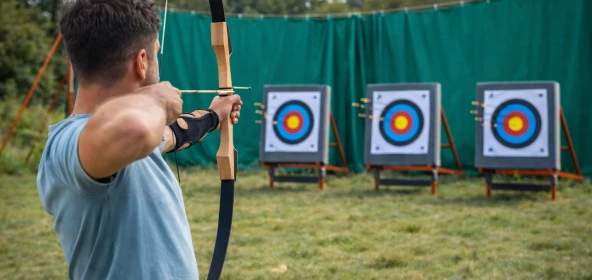 Mann hält einen Bogen in der Hand und zielt den Pfeil auf die Zielscheibe