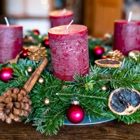 Adventskranz mit Tannengrün, getrockneten Früchten und Zapfen mit dunkelroten Kerzen und kleinen roten Christbaumkugeln