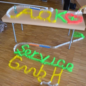 Domino Kette aus gelben, grünen, roten und weißen Steinen, geschrieben AOK Service GmbH